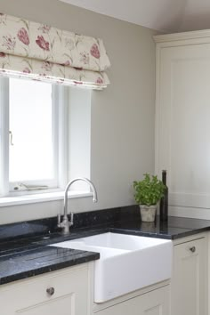 a white kitchen sink sitting under a window next to a counter top with a potted plant