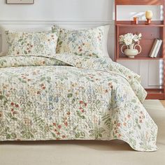 a bed with a floral comforter and pillows on it in a room next to a book shelf