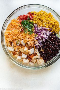 a glass bowl filled with chicken, black beans, corn, and cheese next to tortilla chips