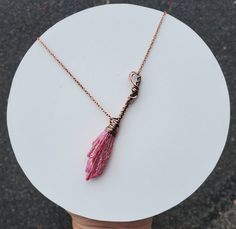 a pink tasseled necklace on a white plate with a hand holding the chain