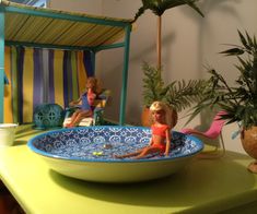 two dolls sitting in a bowl on top of a table next to potted plants