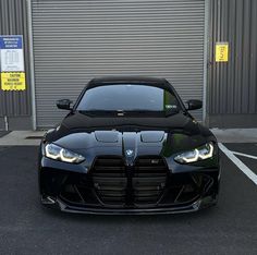 the front end of a black sports car parked in a parking lot next to a building