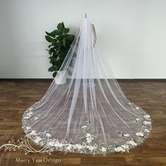 a wedding veil with flowers on the bottom is sitting in front of a potted plant