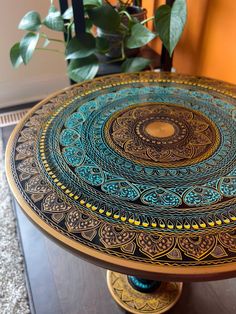 a round table with an intricate design on it and a potted plant in the background