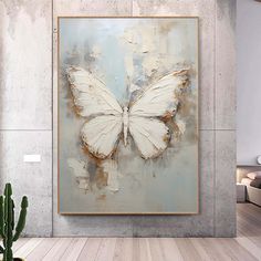 a large white butterfly is hanging on the wall above a plant in a living room