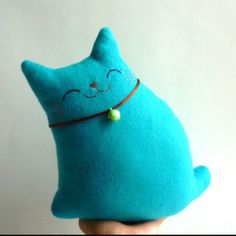 a hand holding a blue stuffed animal with a green bead around it's neck