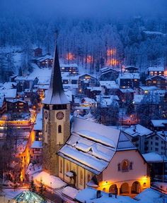 a snowy town is lit up at night with lights on and buildings in the foreground