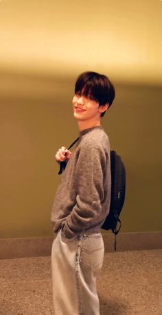 a young boy standing in front of a wall with a backpack on his back and smiling at the camera