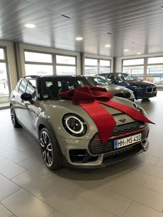 a car with a red bow on the hood is parked in a showroom filled with other cars