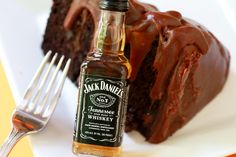 a piece of chocolate cake on a plate next to a fork and bottle of jack daniels