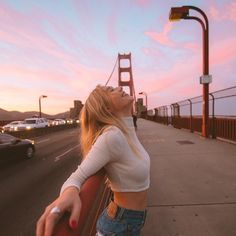 a woman standing on the side of a road next to a bridge