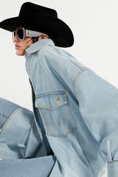 a woman wearing a black cowboy hat and sunglasses sitting on the ground with her legs crossed