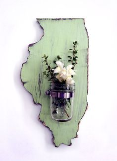 a mason jar with flowers in it mounted on a wooden state shaped wall hanging ornament