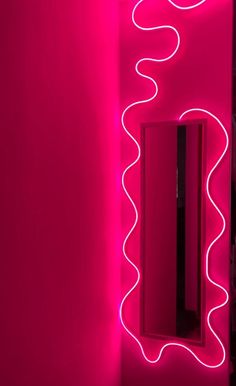 a bathroom with a pink wall and neon lights on the walls, along with a mirror