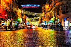 a city street filled with lots of traffic next to tall buildings covered in christmas lights