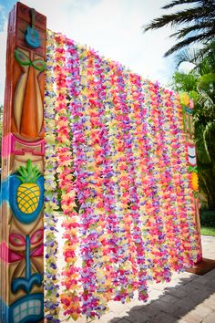 a colorfully decorated wooden pole with flowers and pineapples hanging from it's sides