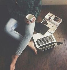 a woman sitting on the floor with her legs crossed holding a coffee cup and laptop