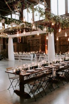 a long table with candles and greenery is set up in an industrial building for a wedding reception