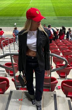 a woman standing in the stands at a baseball game wearing a red hat and black jacket