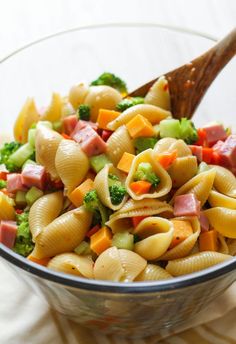 a pasta salad with ham, broccoli and carrots in a glass bowl