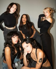 four beautiful young women posing together in black tops and denim pants with tattoos on their arms