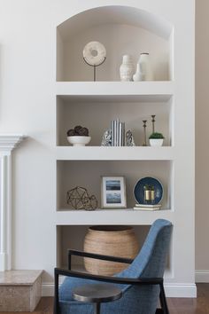 a blue chair sitting in front of a white shelf filled with vases and other items