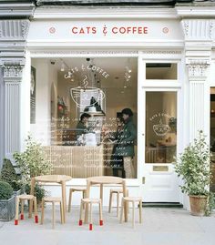 two people standing in front of a coffee shop with tables and chairs on the sidewalk