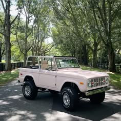 a pink truck parked on the side of a road next to some green trees and grass