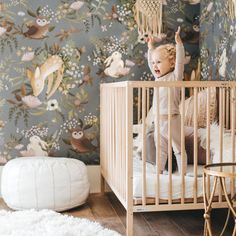 a baby in a crib next to a wallpapered with owls and flowers