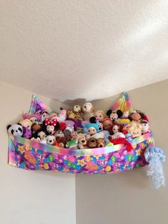 a bunch of stuffed animals are in a basket on the ceiling above a bed with pillows