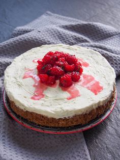 a cake with white frosting and raspberries on top sitting on a plate