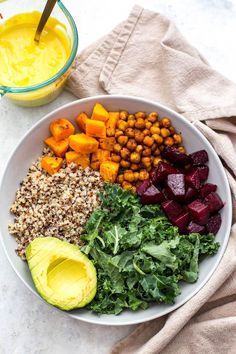 a white bowl filled with greens, carrots and chickpeas next to a glass of orange juice