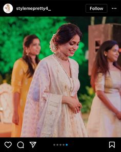 two women standing next to each other in front of some trees and bushes, one woman is wearing a white sari