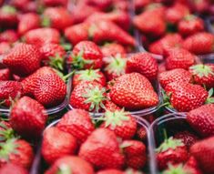 strawberries in plastic containers on display at a fruit stand, with the tops slightly down