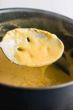 a ladle full of cheese sauce being held by a wooden spoon