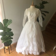 a white wedding dress sitting on top of a wooden floor next to a potted plant