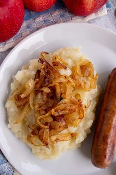 a plate with mashed potatoes, sausage and apples next to it on a table