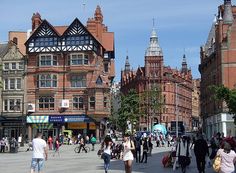 many people are walking on the street in front of some old buildings and tall towers