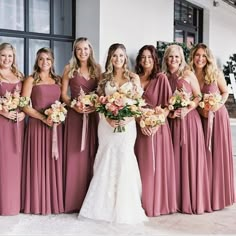 a group of women standing next to each other wearing dresses and holding bouquets in their hands