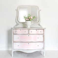 a white dresser with flowers on top and a mirror above it, against a white wall