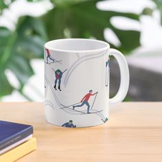 a coffee mug with skiers on it sitting on a table next to a book