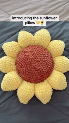 a yellow and red knitted sunflower pillow on a gray bed with the words,'introduce the sunflower pillow'above it