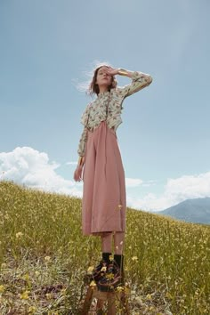 a woman standing on top of a lush green field next to tall grass and flowers