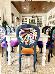 a dining room table with colorful chairs around it