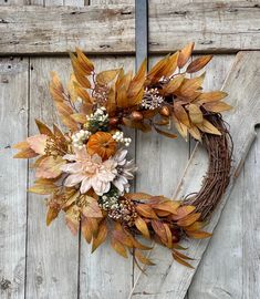 a wreath made out of leaves and flowers on a wooden door with the word fall written in it