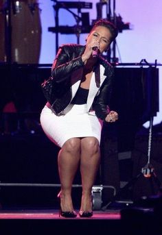 a woman in a white dress and black jacket on stage with her hand up to her mouth