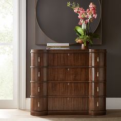 a wooden dresser with flowers on top and a mirror above it in a living room