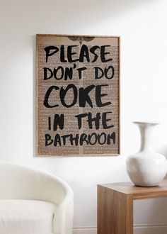 a white vase sitting on top of a wooden table next to a sign that says please don't do cake in the bathroom