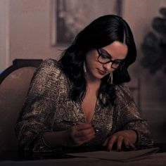 a woman sitting at a table with a pen and paper in her hand, writing