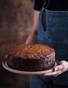 a person in an apron holding a cake on a plate with one hand and the other